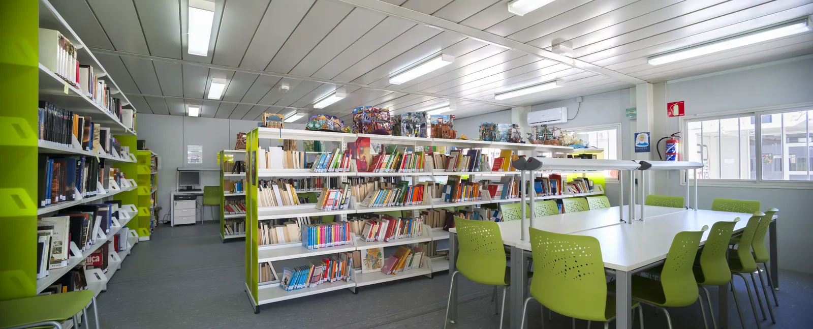 Biblioteca in un edificio modulare con scaffali di libri, tavoli e sedie verdi