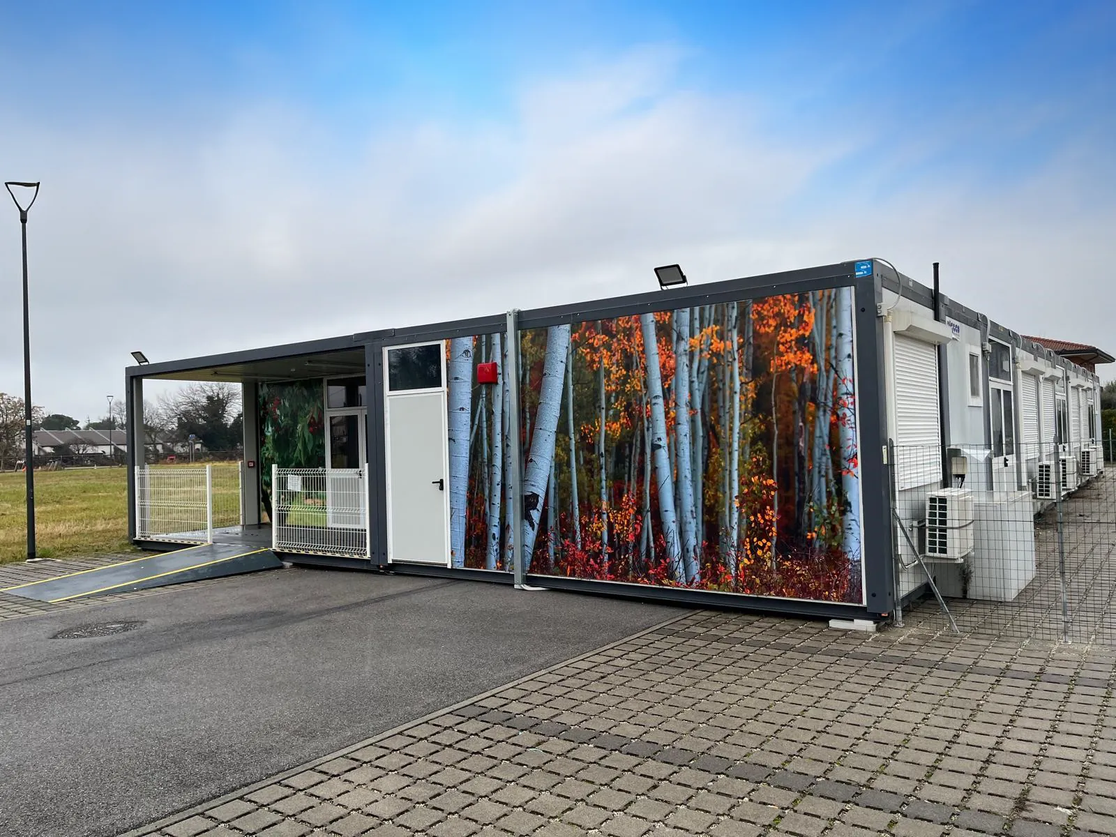 Edificio modulare con pannello decorato a bosco di betulle e ingresso coperto con rampa