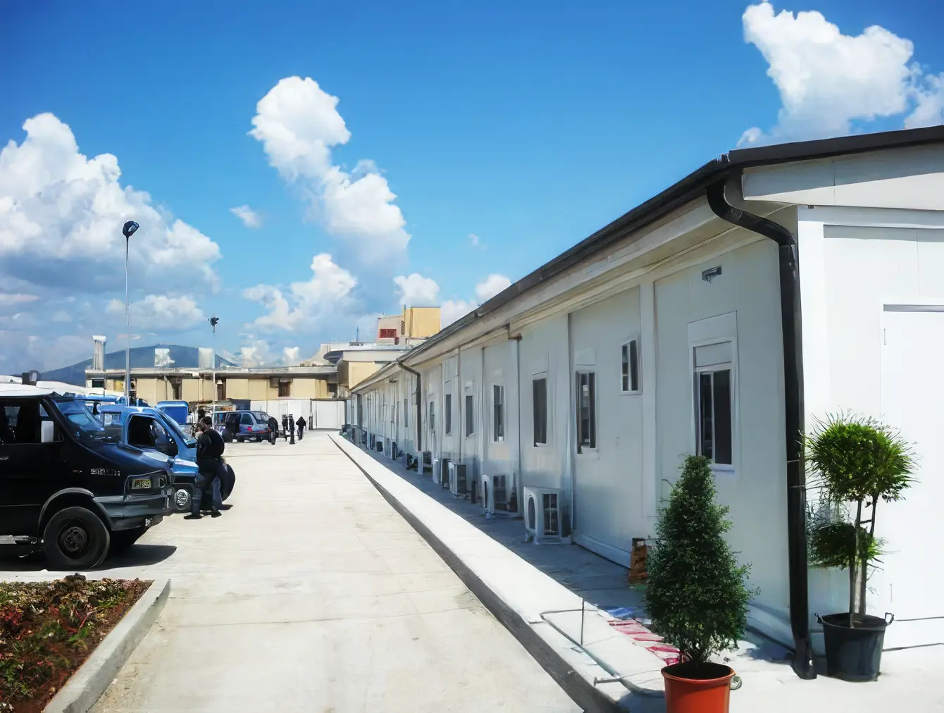 Fila di moduli prefabbricati bianchi Algeco con piante in vaso e veicoli di servizio nel piazzale