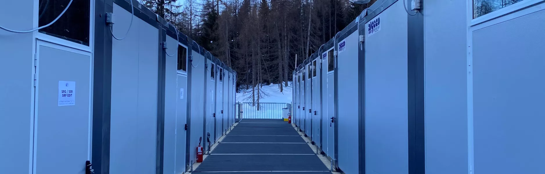 Corridoio tra moduli abitativi allineati in un campo innevato