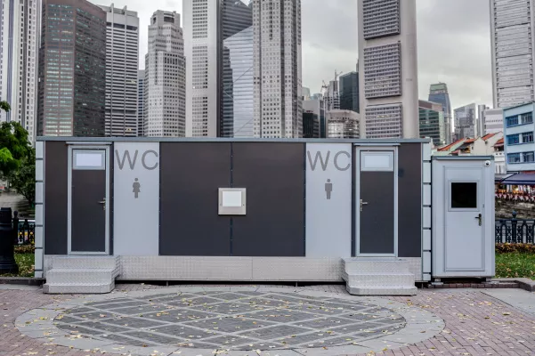 Blocco wc prefabbricato in una piazza con grattacieli sullo sfondo