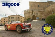 Auto d'epoca rossa parcheggiata davanti a un borgo con castello medievale