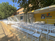 Sedie bianche allineate nell'area ospitalita del festival accanto ai moduli gialli